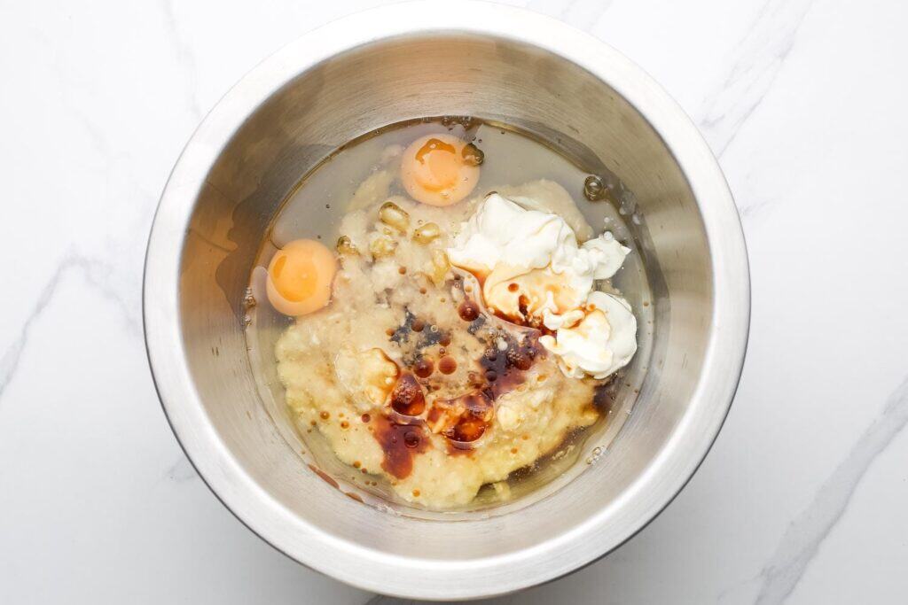 Mixing bowl with mashed bananas, eggs, sour cream, oil, honey or maple syrup, and vanilla before combining.