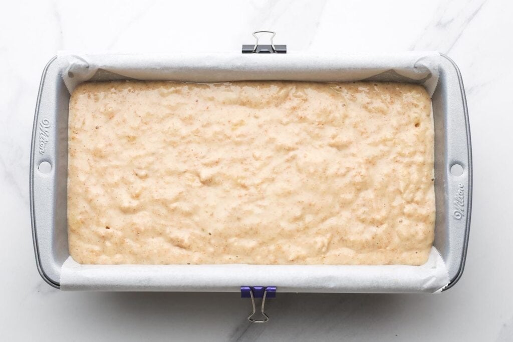 Banana bread batter poured into a lined loaf pan, ready to bake.
