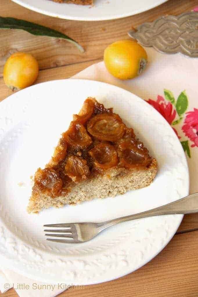 A slice of Loquat Upside Down Cake on a white plate with a fork on the side