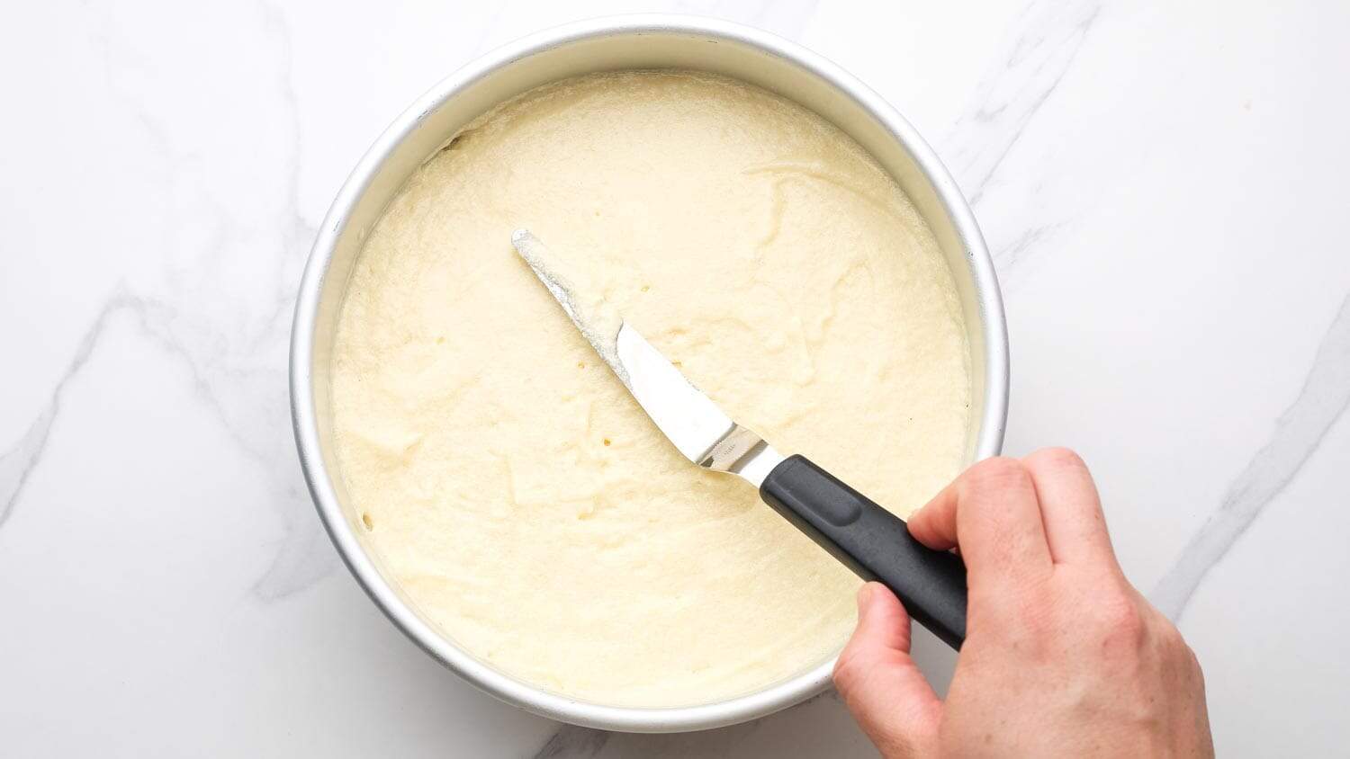 Spreading banana cake batter evenly over caramel layer in cake pan with an offset spatula.