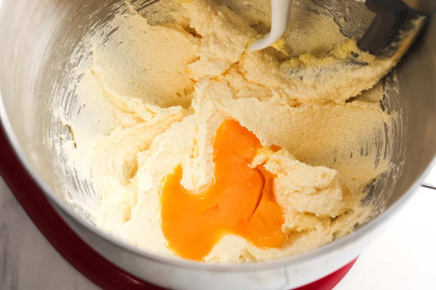 Mixing bowl with cake batter and an added egg yolk on top, ready to be mixed in.