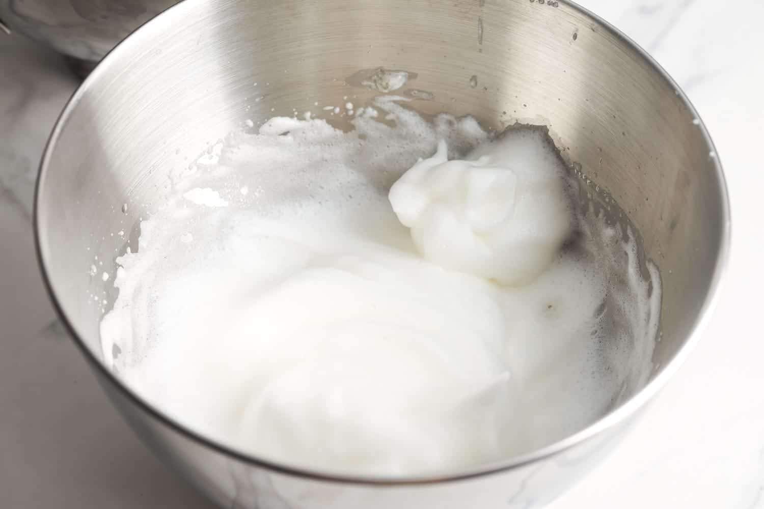 Whipped egg whites in a stainless steel bowl.