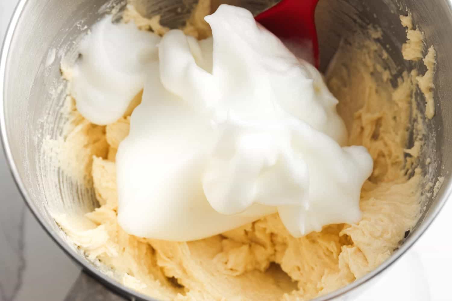 Whipped egg whites added to cake batter in mixing bowl with spatula.