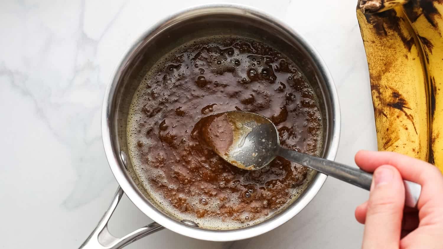 Hand stirring brown sugar mixture into caramel in a saucepan.