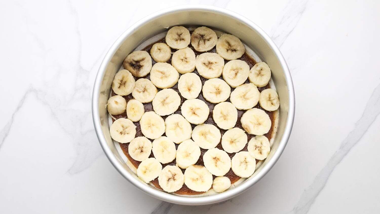Sliced bananas arranged evenly over the caramel layer in a round cake pan.