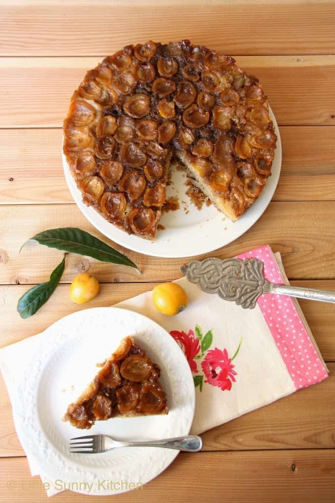 Loquat upside down cake, and a slice of cake served on a white plate with a small cake fork placed over a floral tea towel.