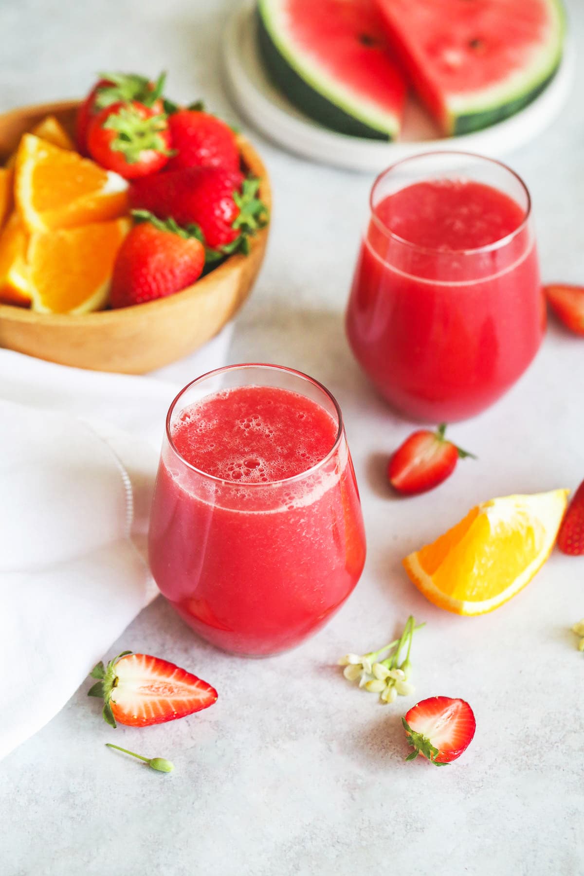 Strawberry Watermelon Smoothie in 2 glasses, and a bowl of fresh strawberries, orange, and watermelon slices.