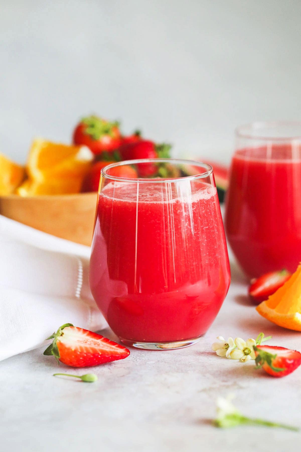 2 glasses of strawberry watermelon smoothie, with fresh strawberry halves and flowers on the counter