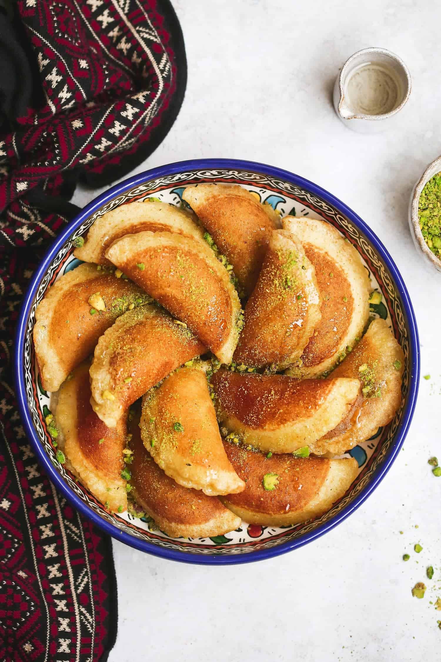 Atayef on a large oriental dish, garnished with ground pistachio