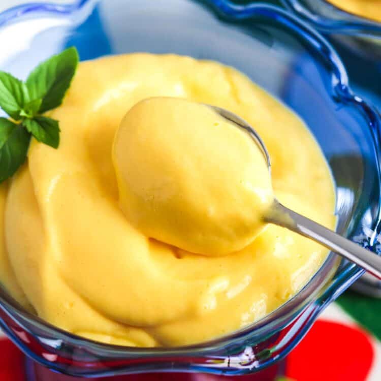 Creamy mango mousse served in a blue dessert cup with a spoon and mint garnish