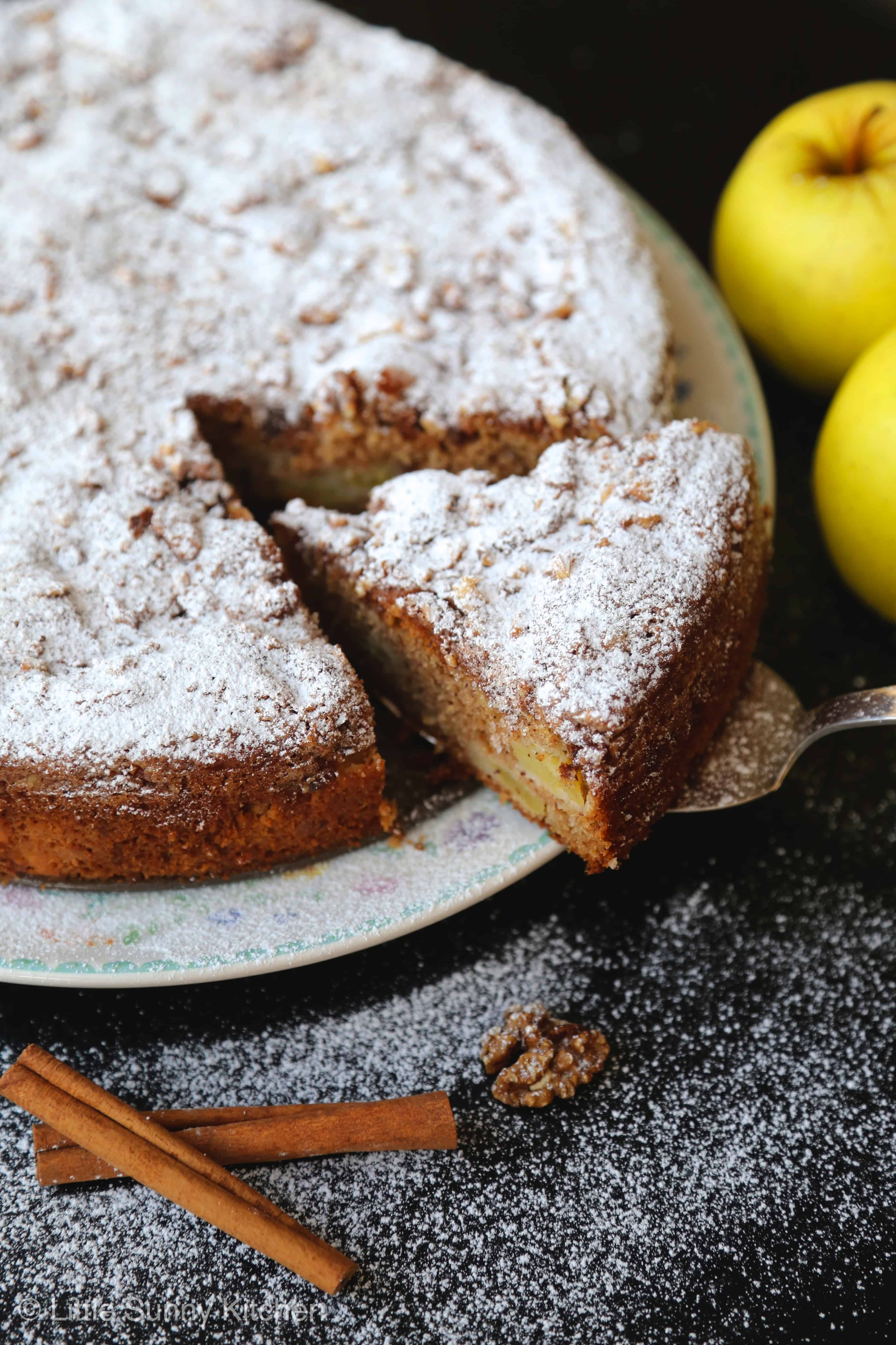 Apple Sharlotka cake topped with powdered sugar with apples and cinnamon sticks on the side. 