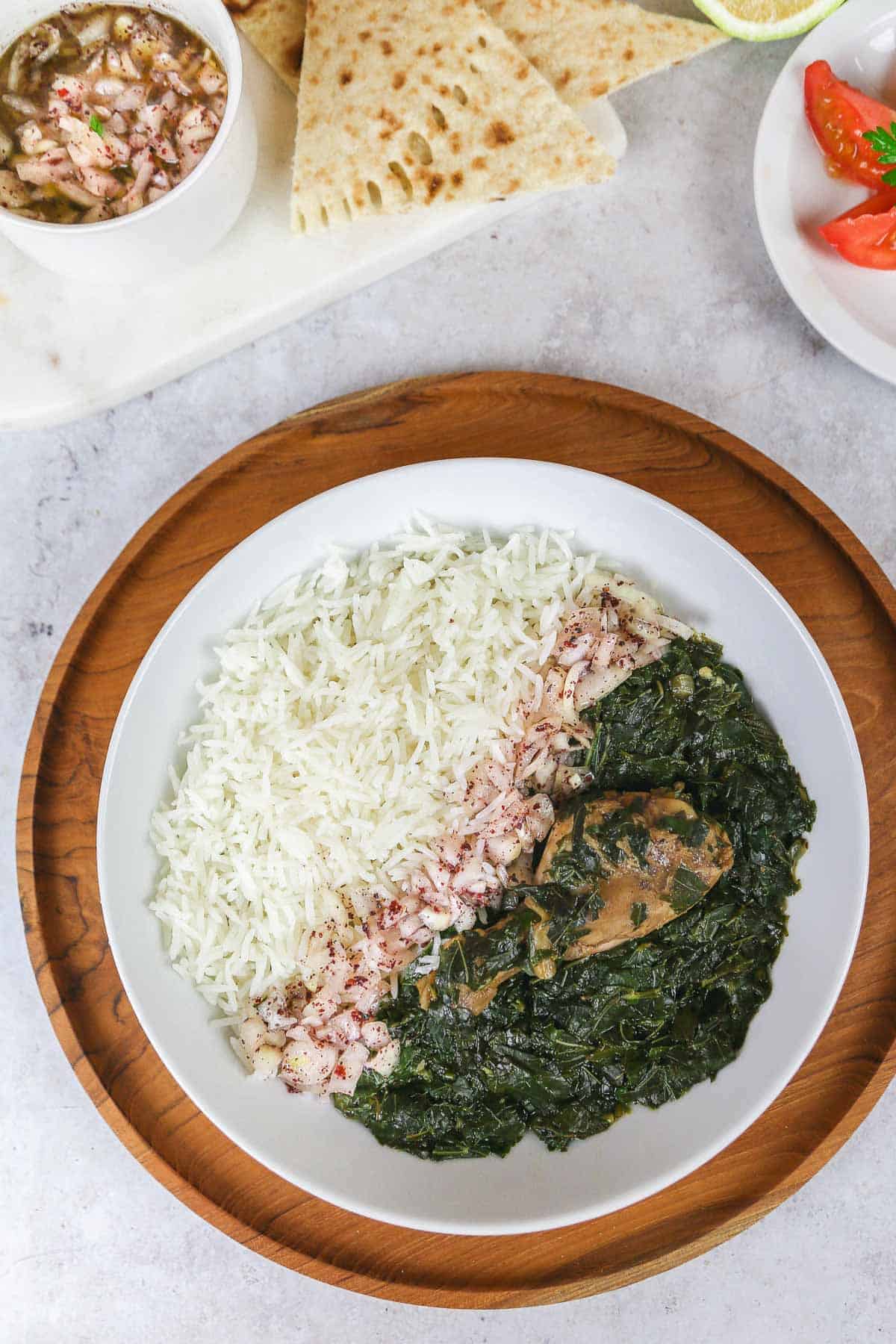 A bowl of molokhia with rice, and a chicken drumstick placed on a wooden tray