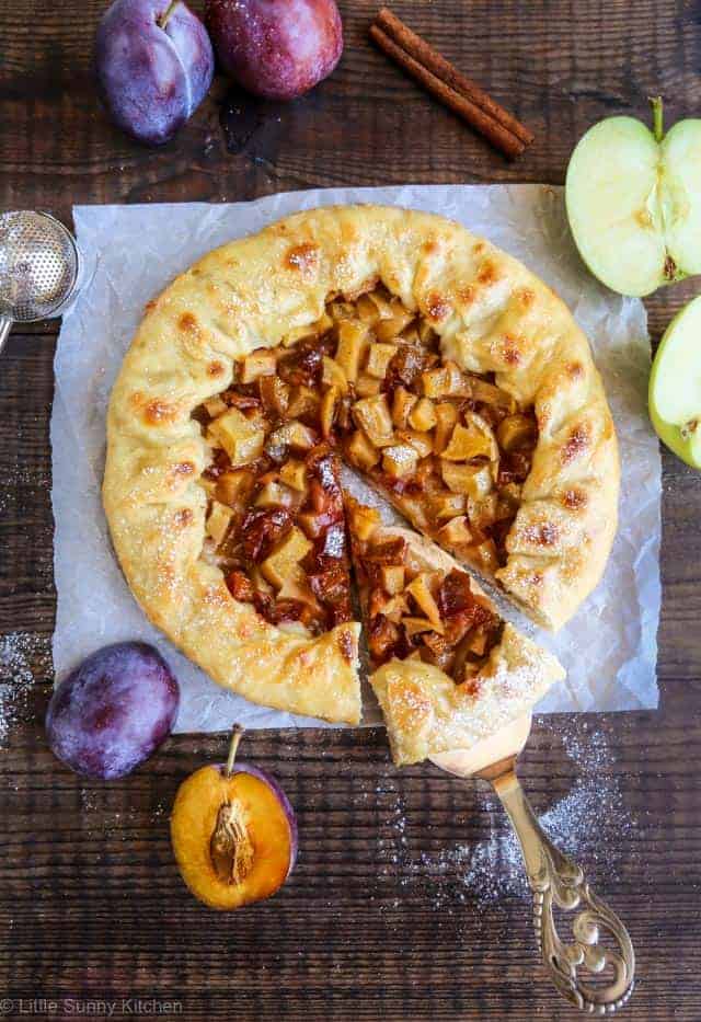 Baked plum apple galette on a parchment on a wooden surface.