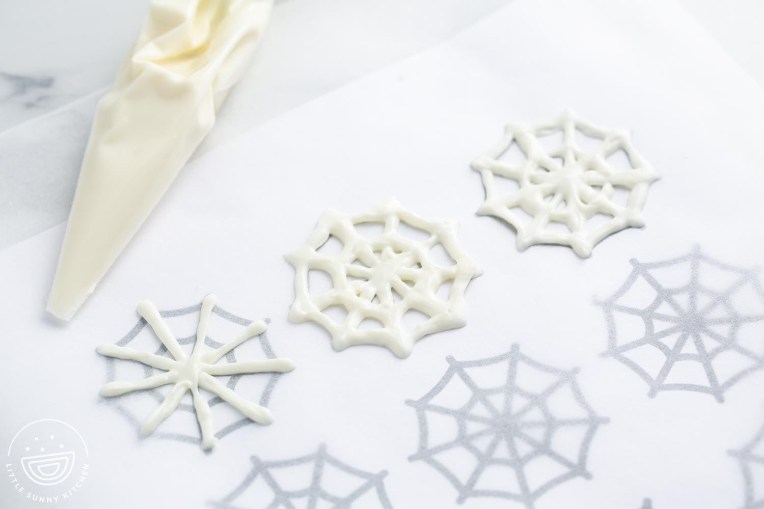 Creating white chocolate spider webs that are piped onto parchment paper with a template underneath it