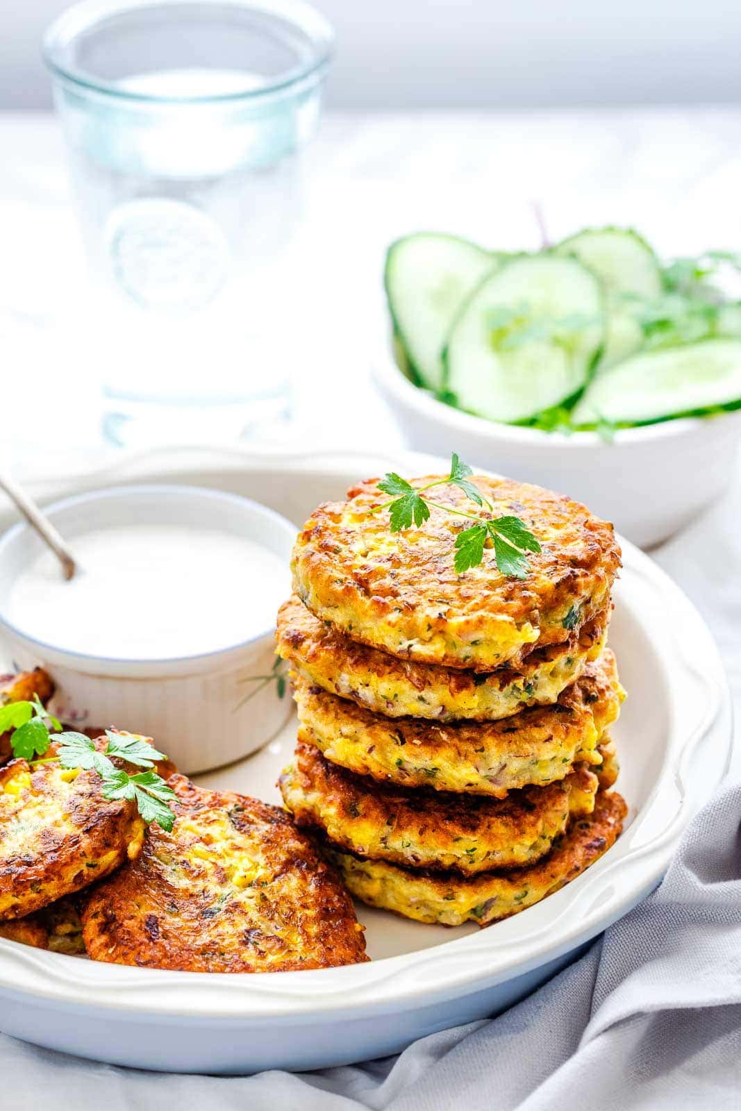 Corn fritters stacked in a white plate, with yogurt sauce on the side