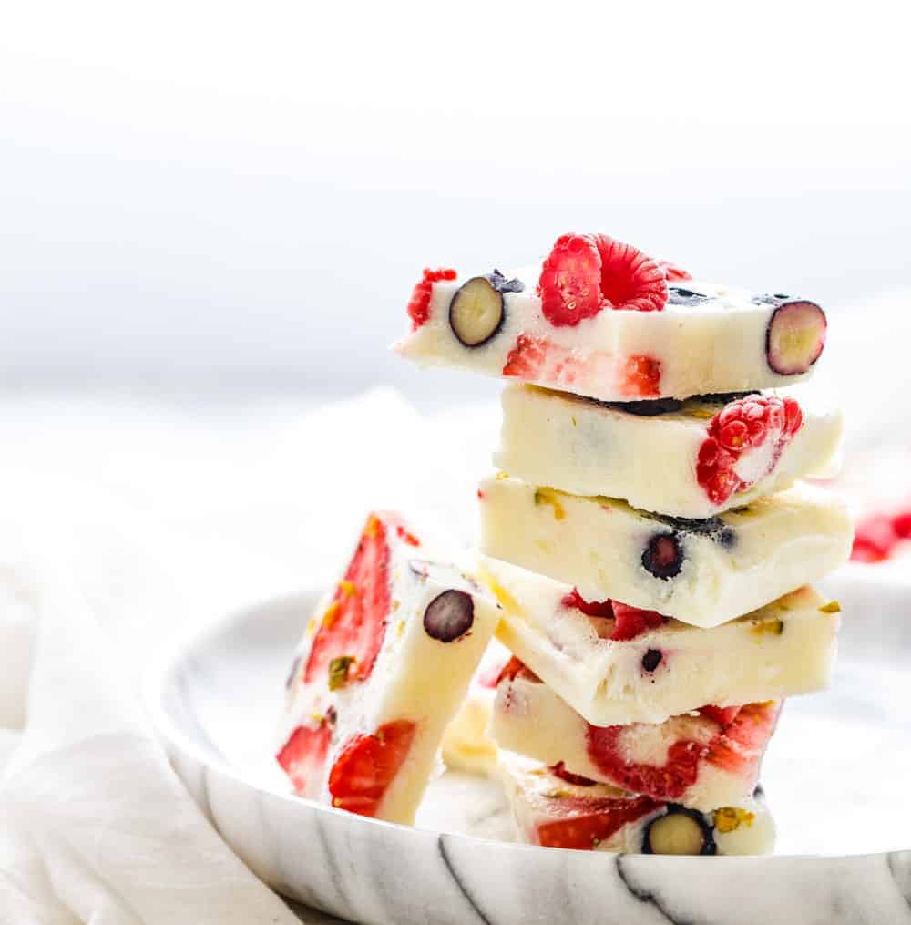 Angle shot of squares of berry frozen yogurt bark stacked on marble plate