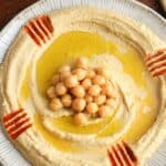 Overhead shot of creamy homemade hummus spread on a plate, topped with a few chickpeas, and olive oil.