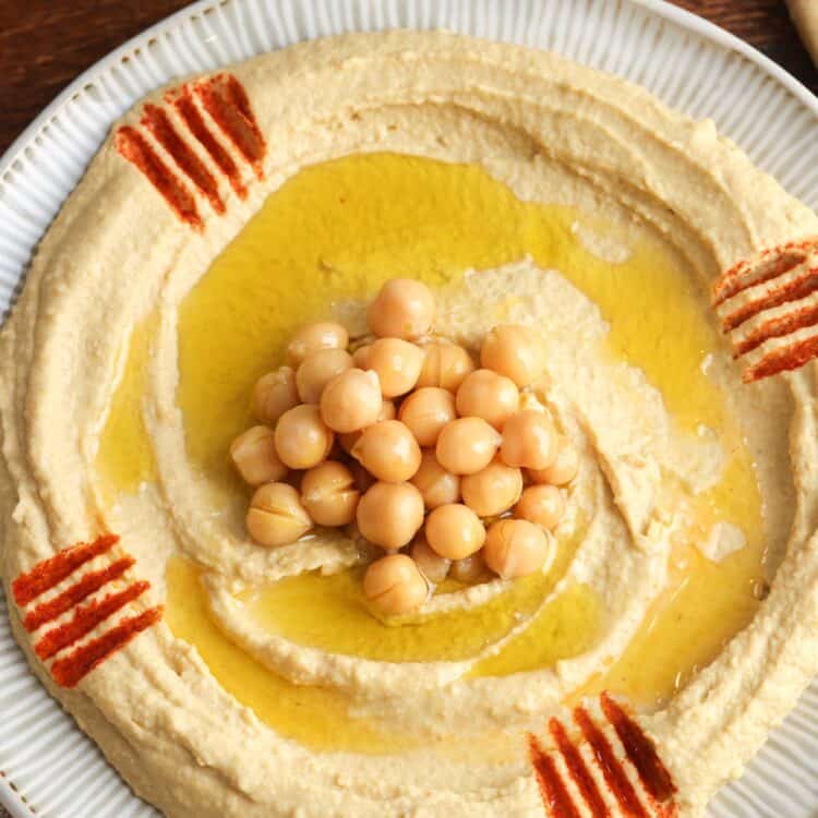 Overhead shot of creamy homemade hummus spread on a plate, topped with a few chickpeas, and olive oil.