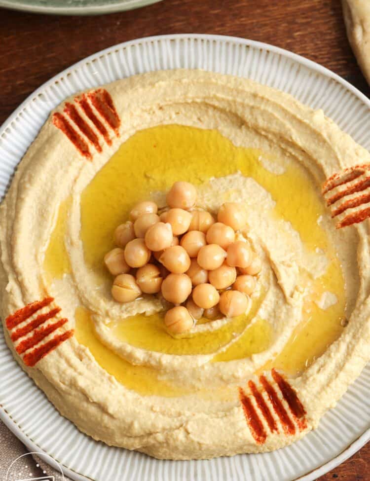 Overhead shot of creamy homemade hummus spread on a plate, topped with a few chickpeas, and olive oil.