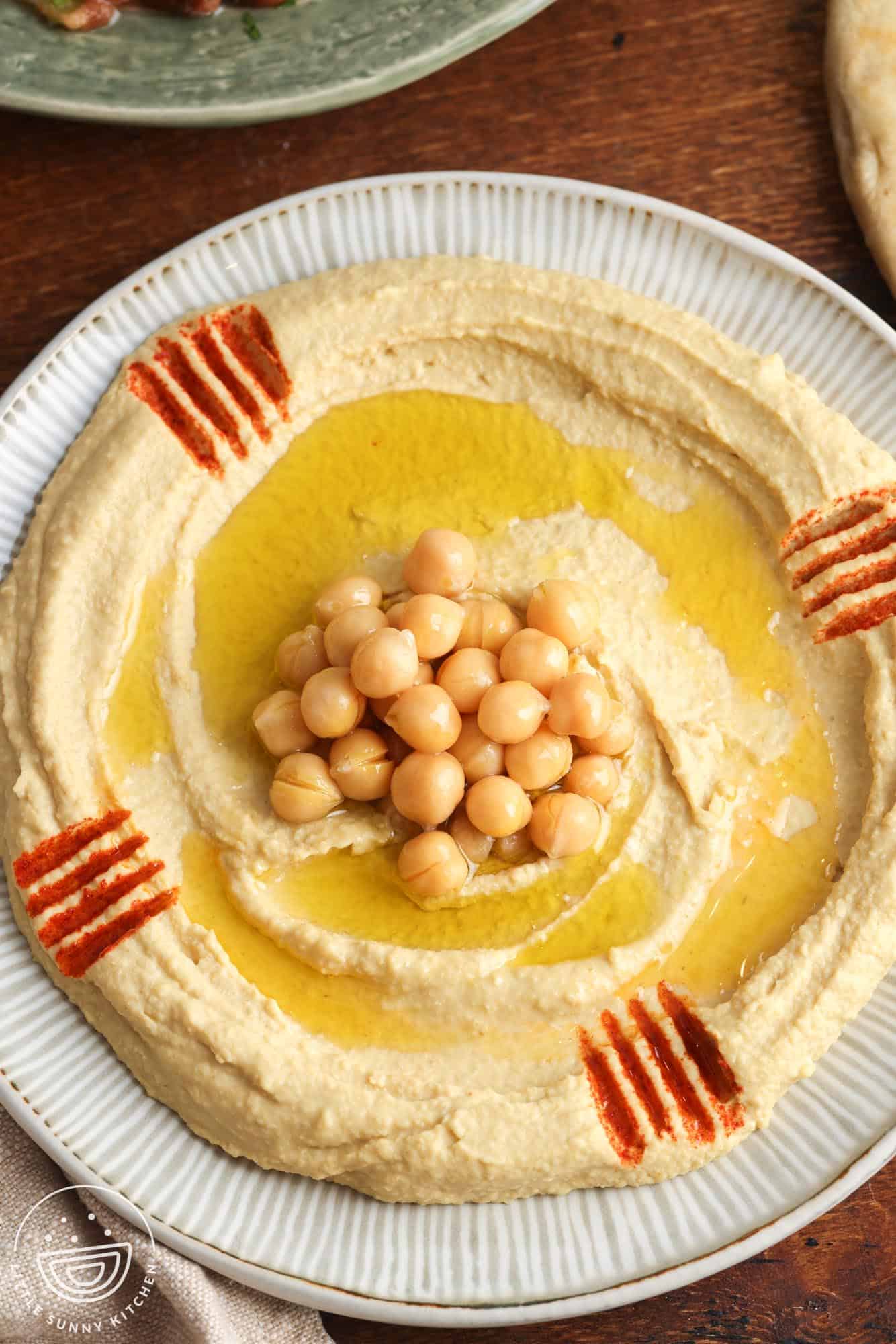 Overhead shot of creamy homemade hummus spread on a plate, topped with a few chickpeas, and olive oil.