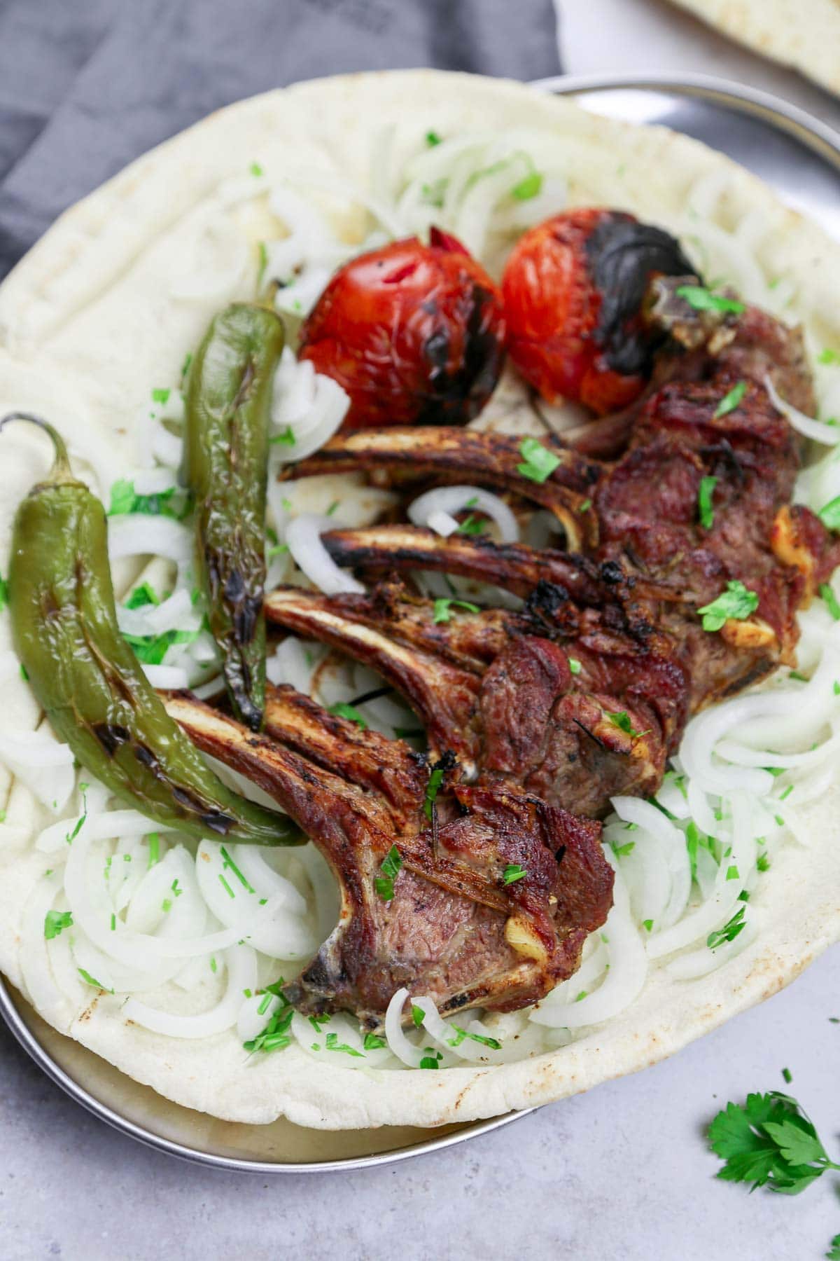 Middle Eastern grilled lamb ribs served over pita bread with charred tomatoes and charred chilis.