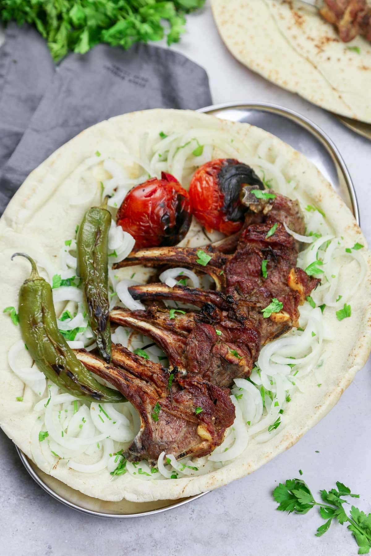 Grilled lamb ribs served over pita bread, sliced white onions, and charred tomatoes and chili peppers