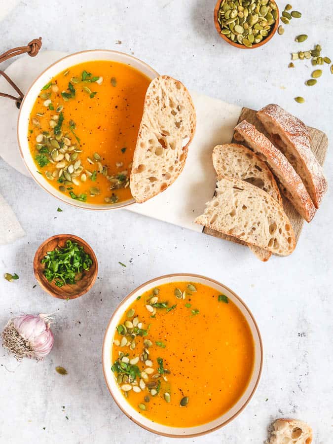 Two bowls of butternut squash soup, with a white marble board and slices of toasted bread.