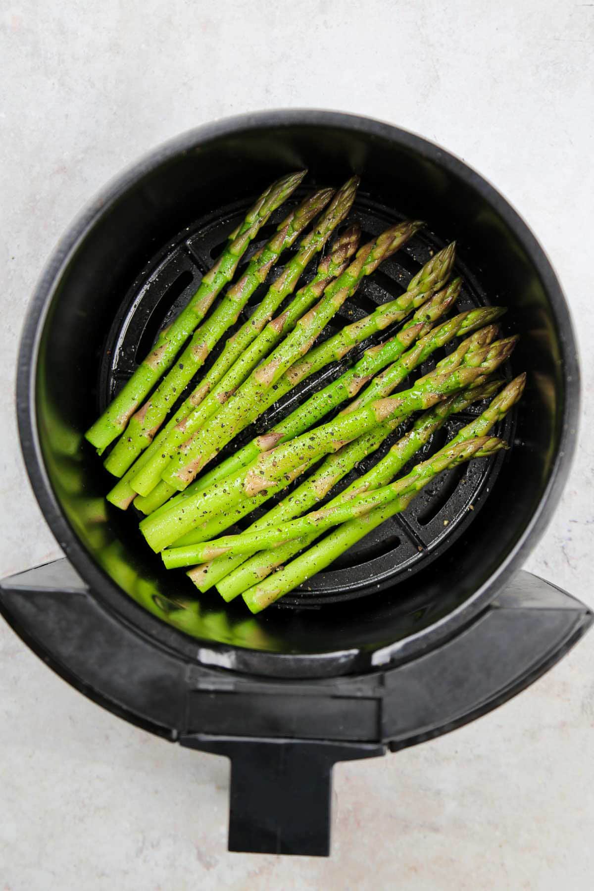 Seasoned and oil-sprayed asparagus tips in the air fryer basket.