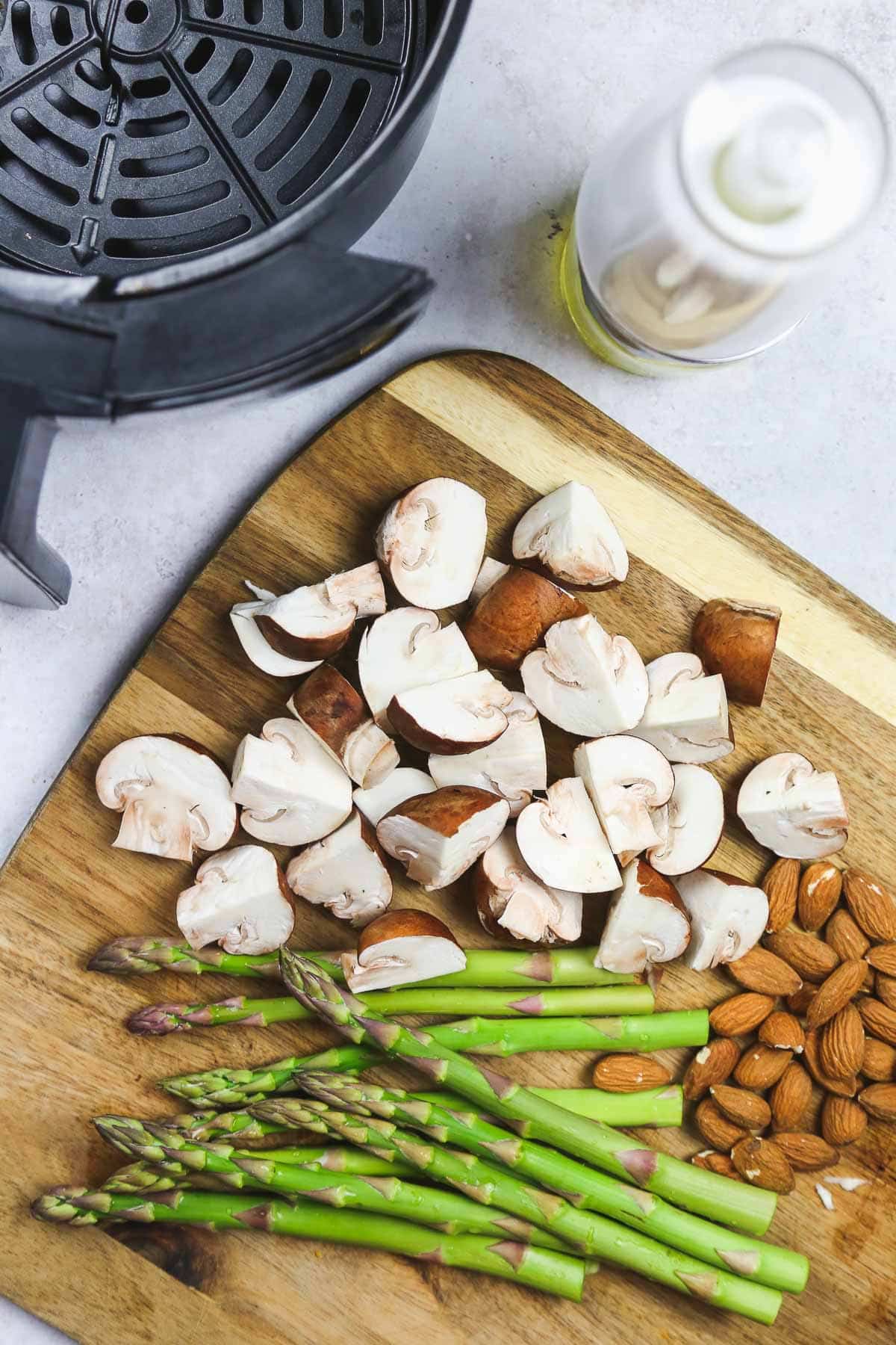 Asparagus with quartered mushrooms and almonds on a wooden cutting board.