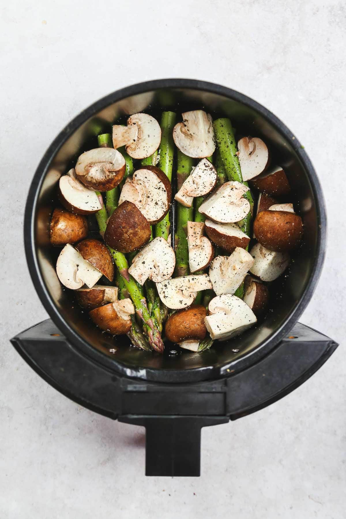 Seasoned and oil-sprayed asparagus and mushrooms placed in the air fryer basket.