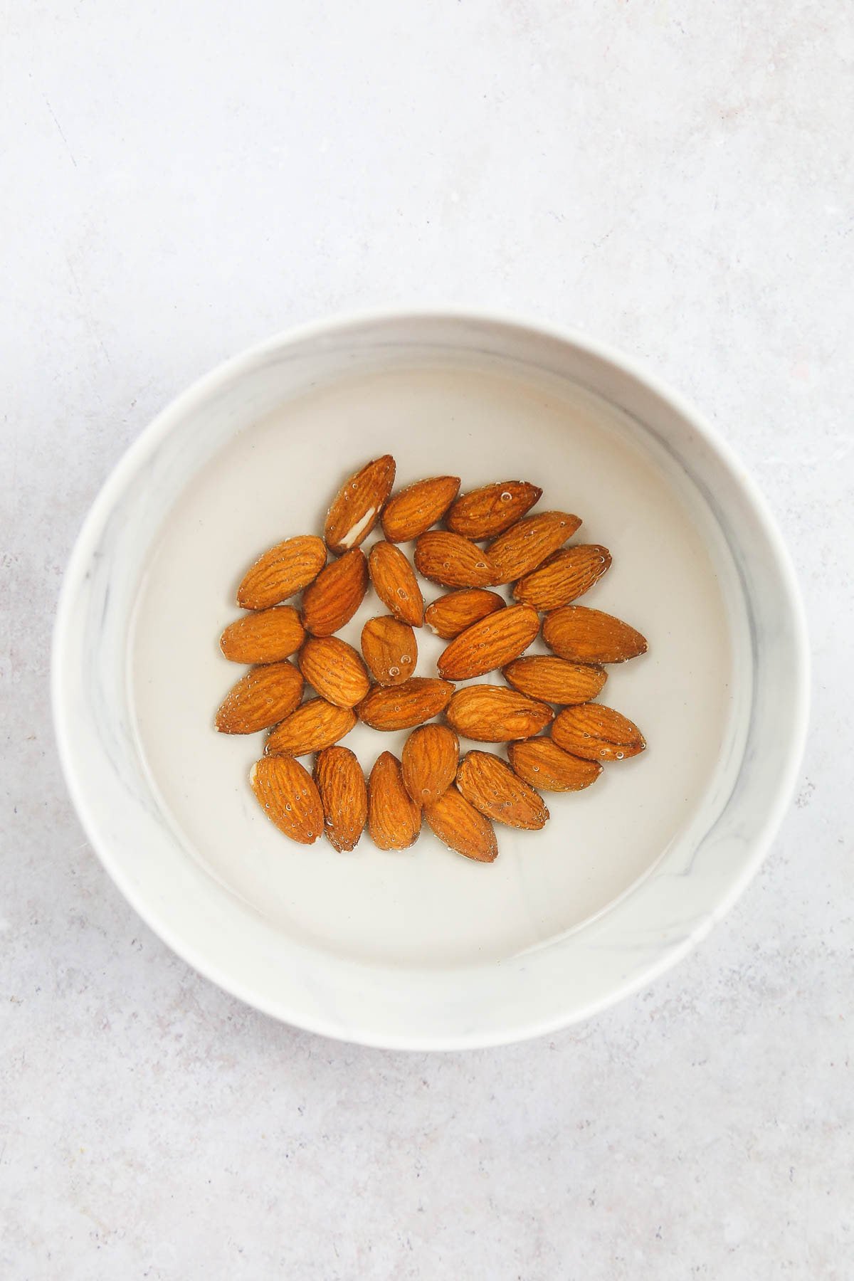 Almonds soaked in water in a white bowl.