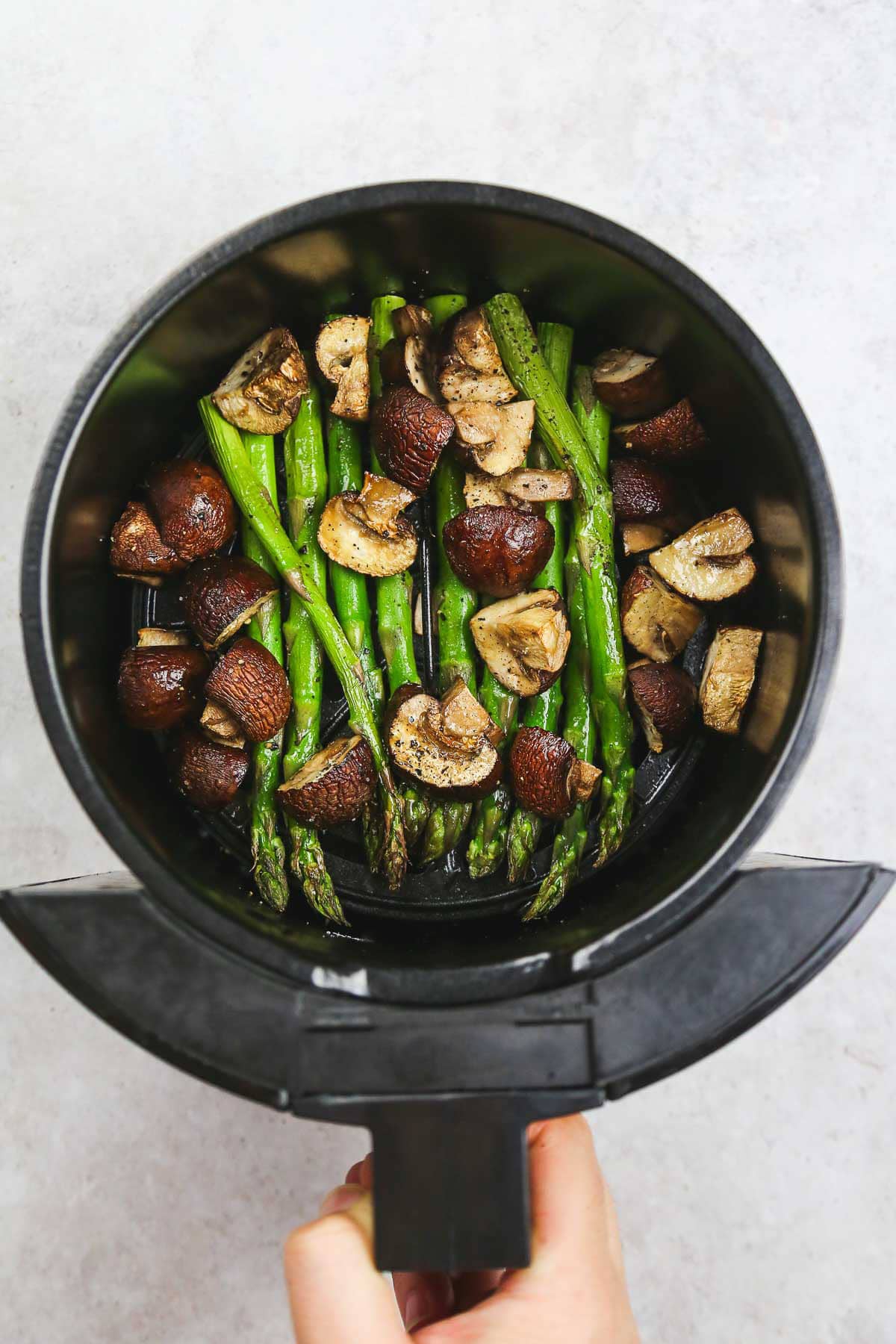 Ready and crispy asparagus and mushrooms in the air fryer basket.