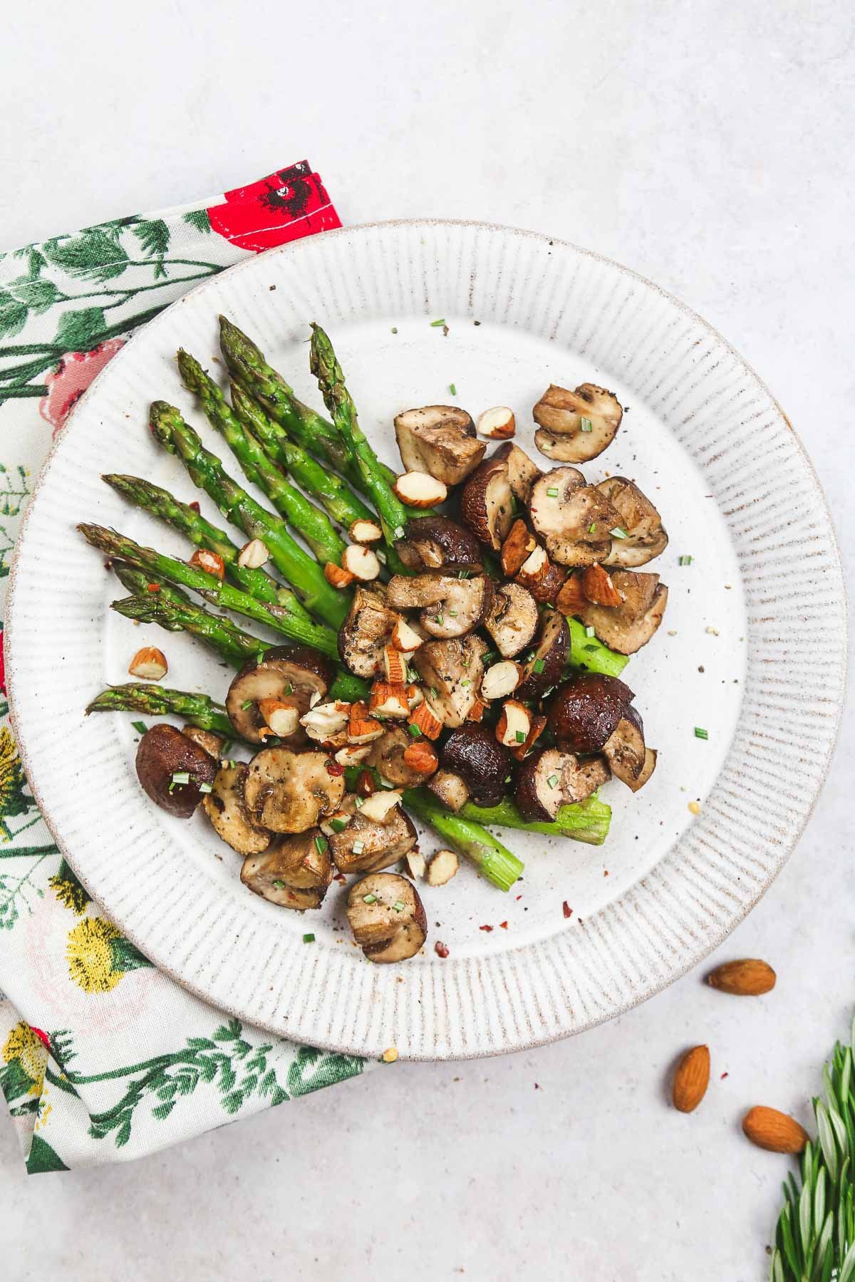 Crispy air fryer Asparagus and mushroom topped with crushed almonds served in a white plate; with a floral tea towel on the side.