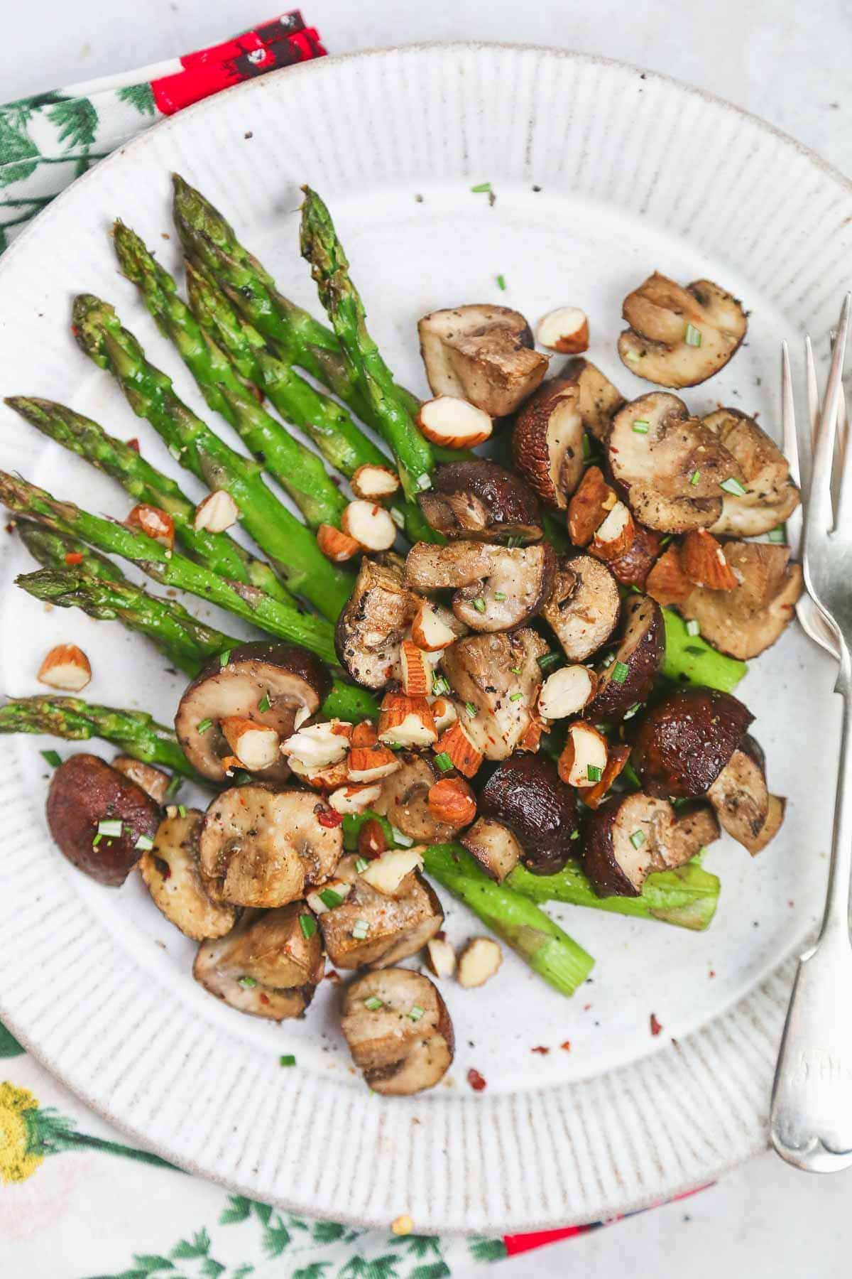 Air fryer asparagus and mushroom topped with crushed almond on a white plate with a fork.