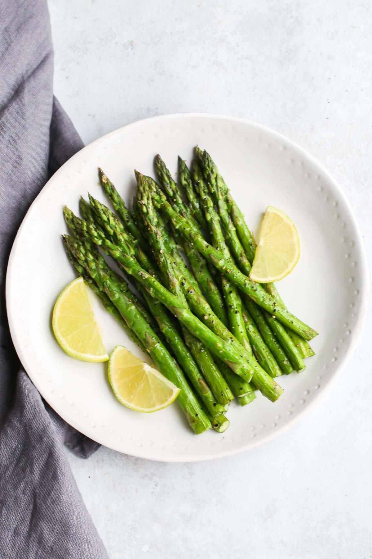 Crispy air fryer asparagus served with lemon wedges on a white plate.