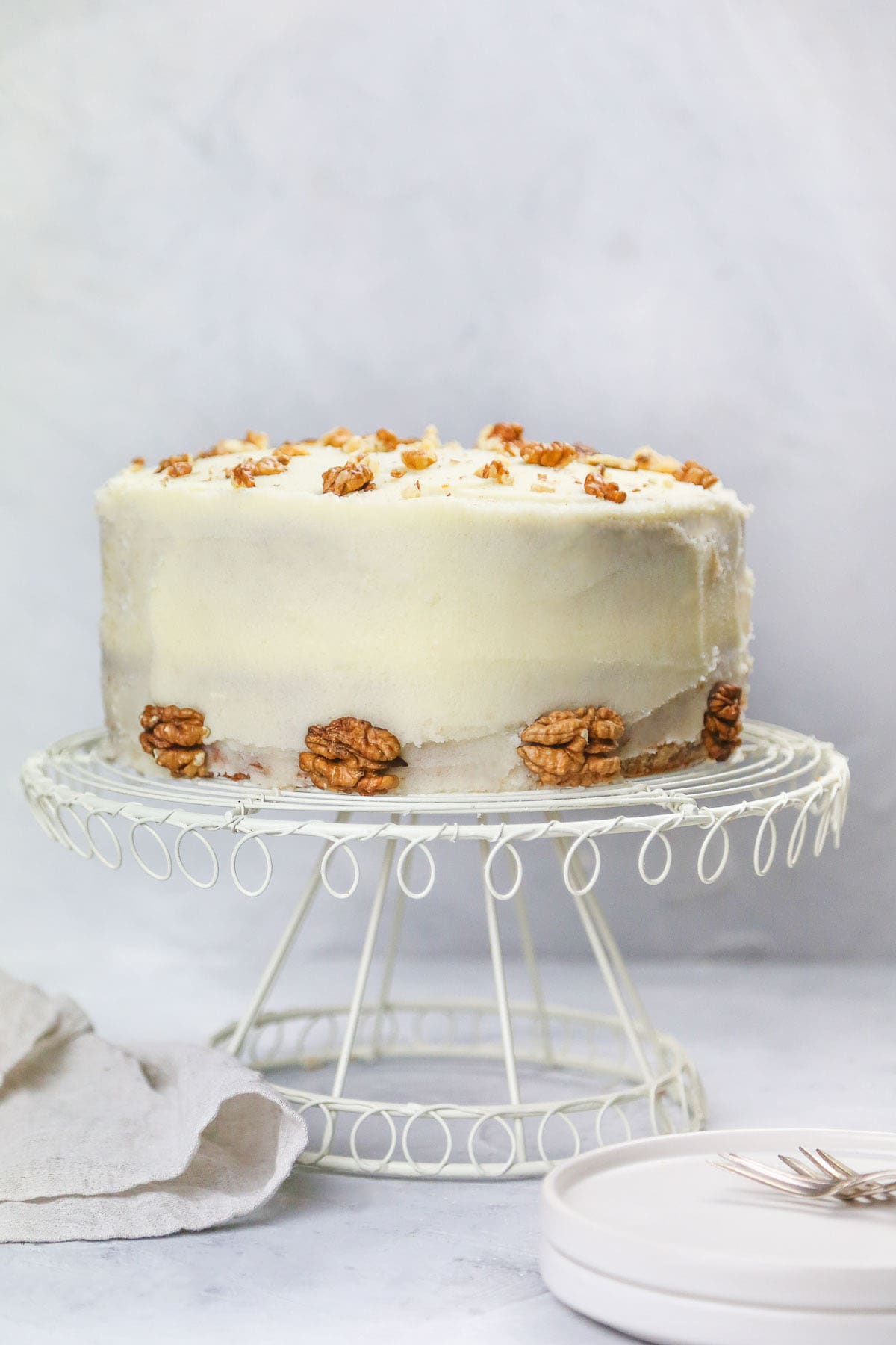 Frosted banana cake on a wired cake stand with walnuts