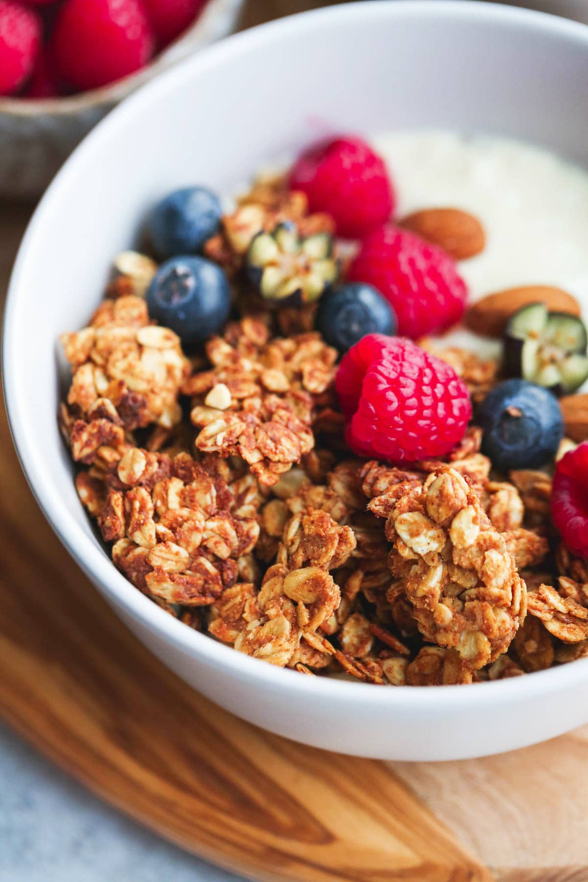 A close up shot of granola clusters in a bowl with fresh raspberries and blueberries
