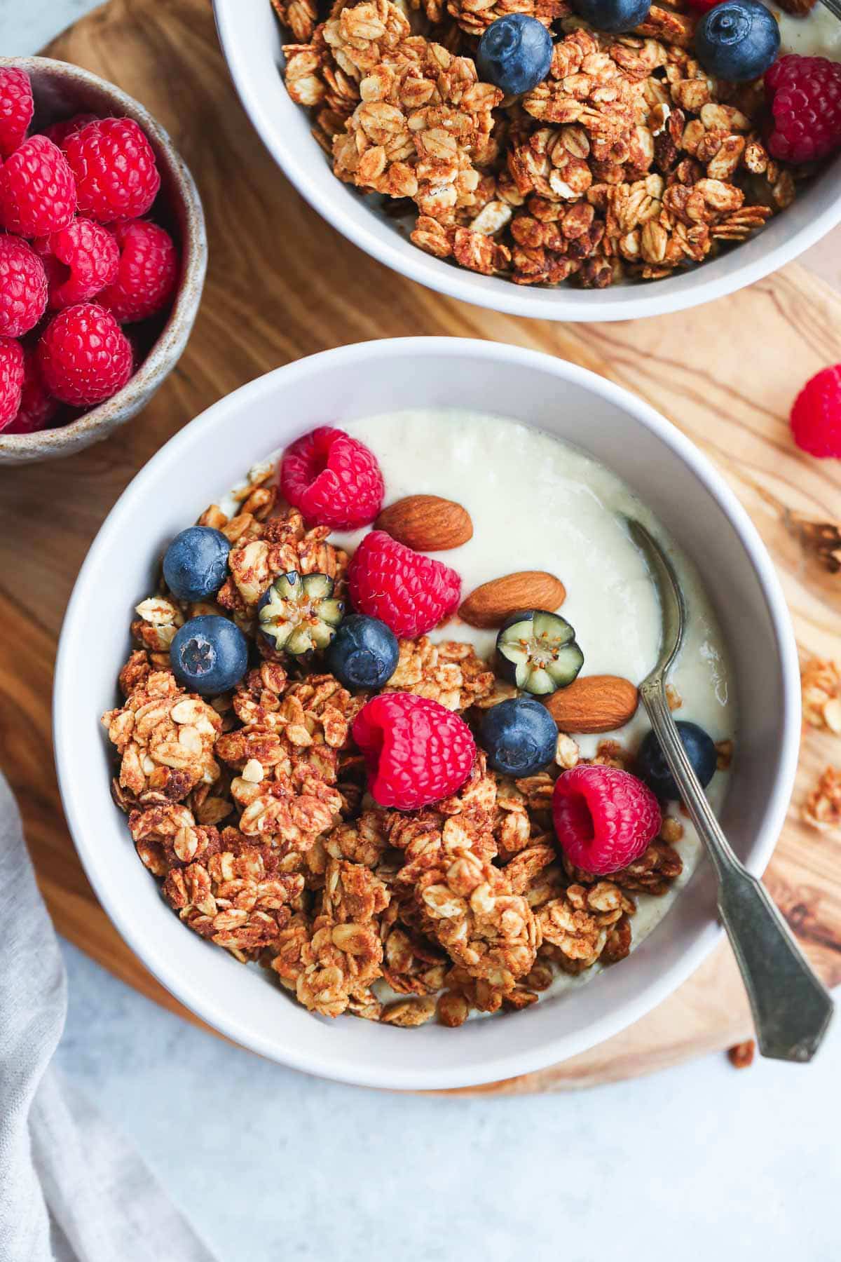 A bowl of peanut butter granola with soy yogurt and fresh berries, on a wooden board