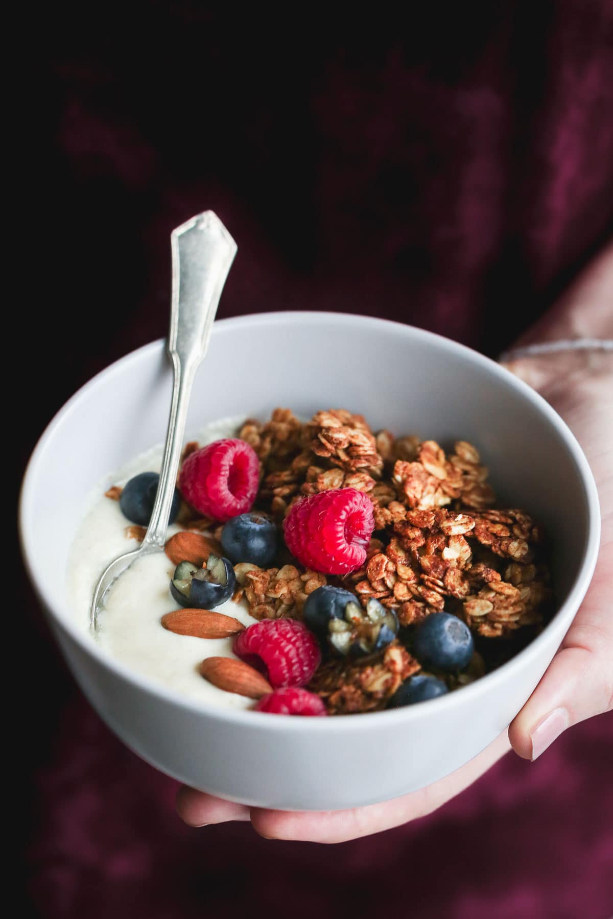 Holding a bowl of yogurt with granola and fruit, with a teaspoon