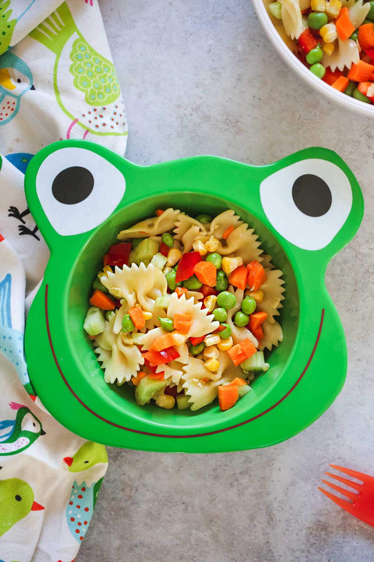 Pasta salad in a fun kids frog shaped bowl and a plastic red fork on the side