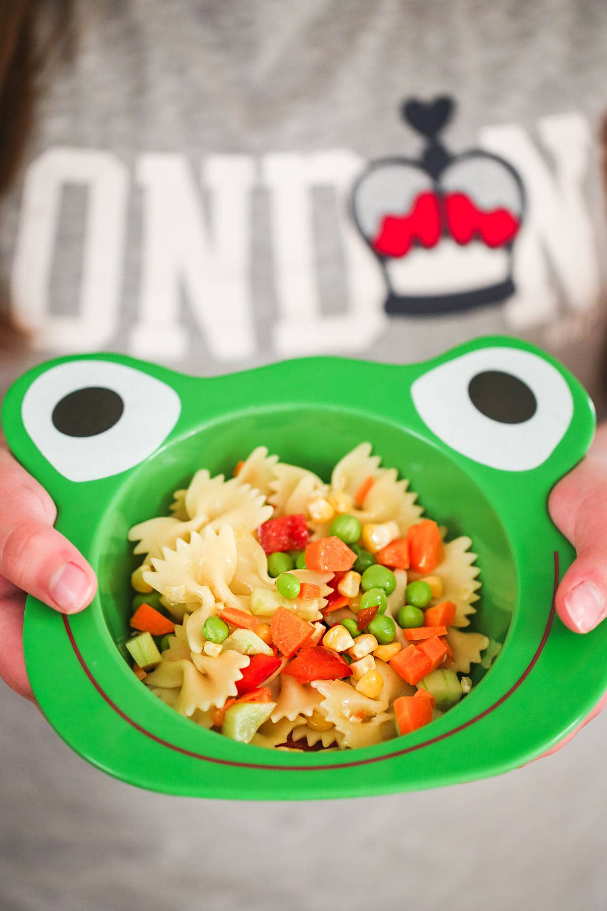 A girl holding a fun frog shaped bowl filled with pasta salad