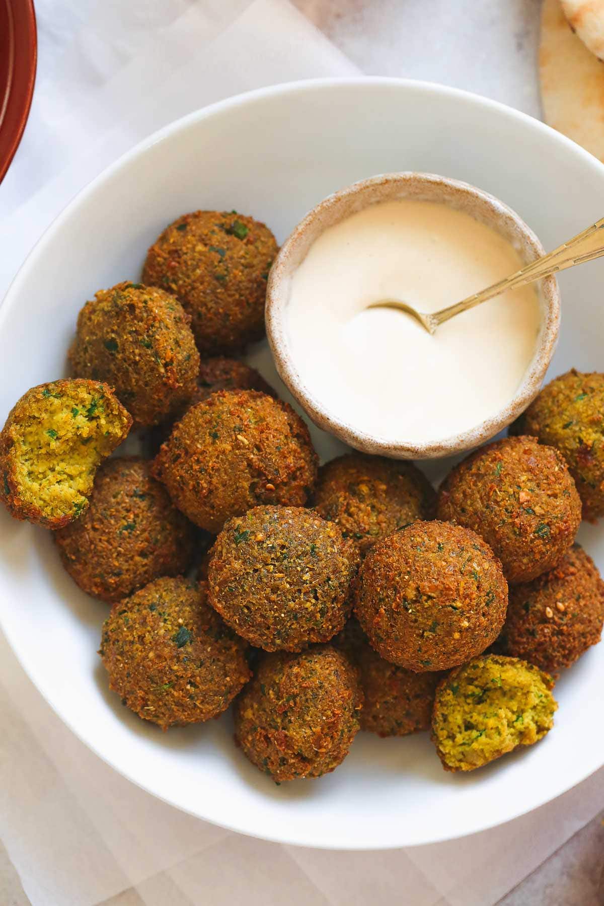 A close up picture of traditional round falafel balls in a bowl with tahini sauce