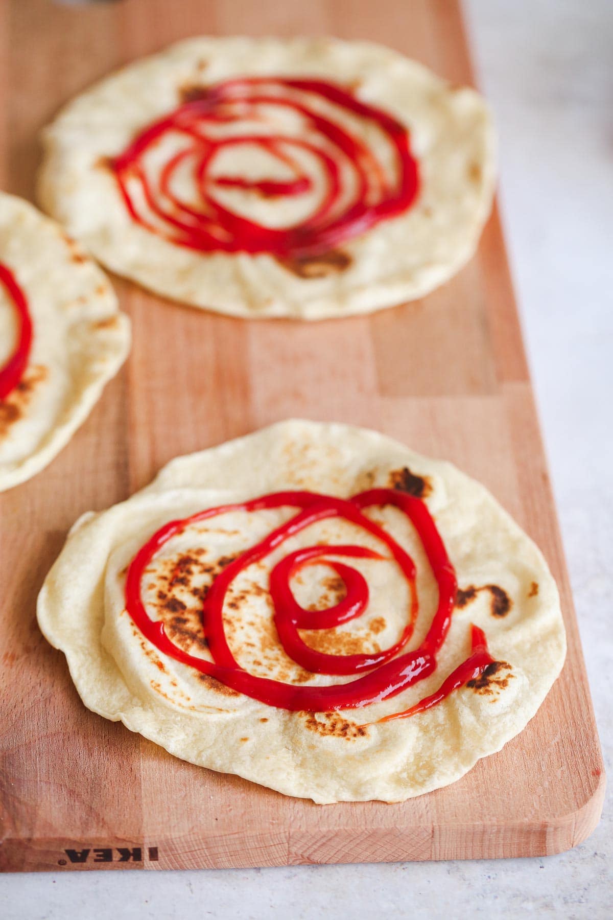 Flatbread with ketchup on top, laid on an IKEA wooden chopping board