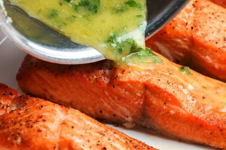 Close-up of garlic butter lemon sauce being poured over cooked salmon fillets.