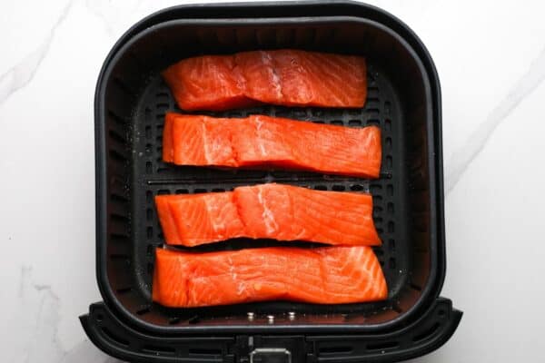 Uncooked salmon fillets placed in an air fryer basket before cooking.