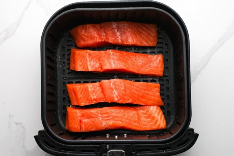 Uncooked salmon fillets placed in an air fryer basket before cooking.
