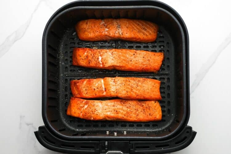 Golden cooked salmon fillets sitting in an air fryer basket.