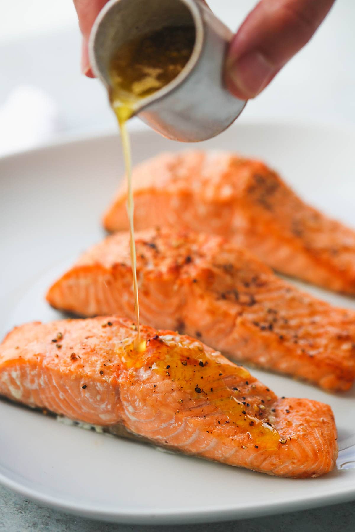 Pouring garlic lemon butter sauce over perfectly cooked air fryer salmon fillets.