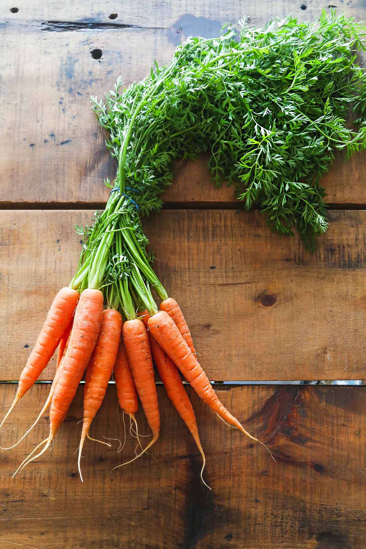 Organic carrots with green tops on a wooden table surface