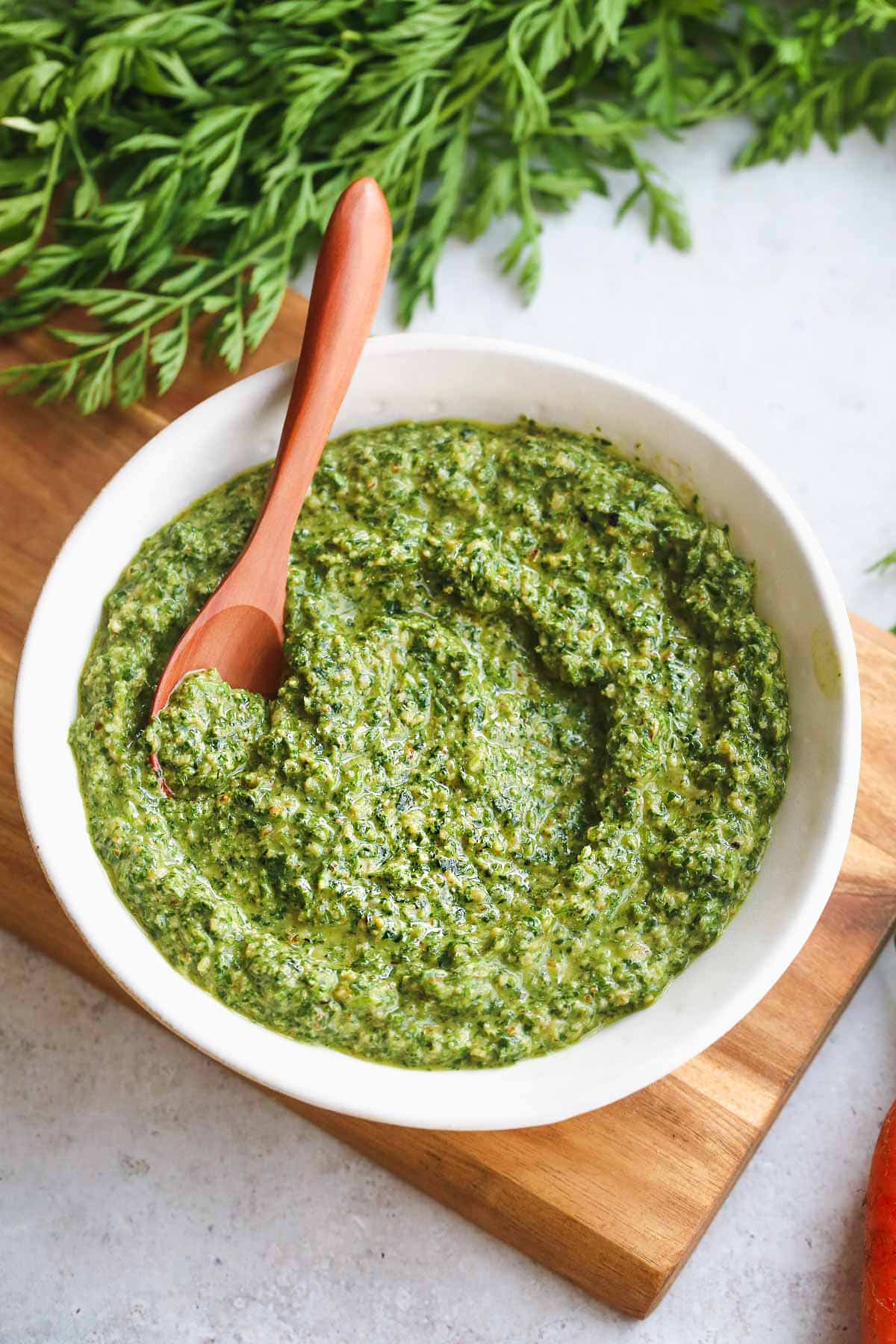 Carrot Top Pesto in a white bowl and a small wooden spoon